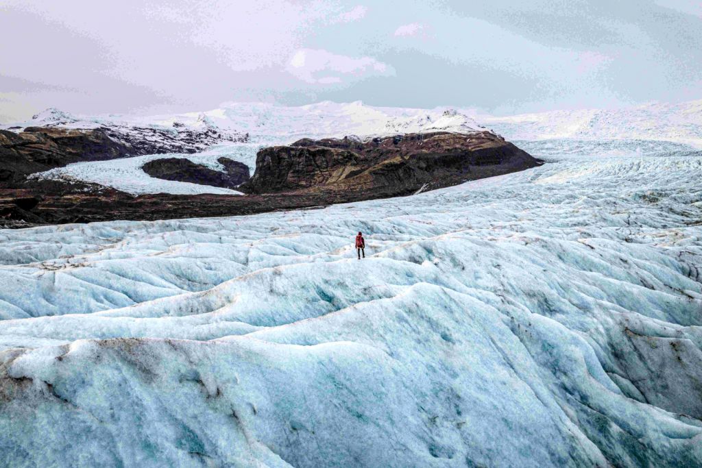 Person in distance, standing on a glacier with a small mountain in a further distance.