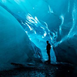 Man standing inside a blue ice cave.