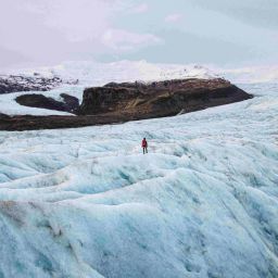A lone tourist walking on a glacier in Iceland, surrounded by beautiful views.