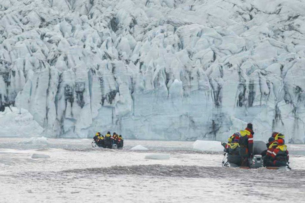 Tourists on a boat against the backdrop of a glacier wall.