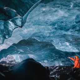 A person expering an ice cave from within and pointing to the cave opening.