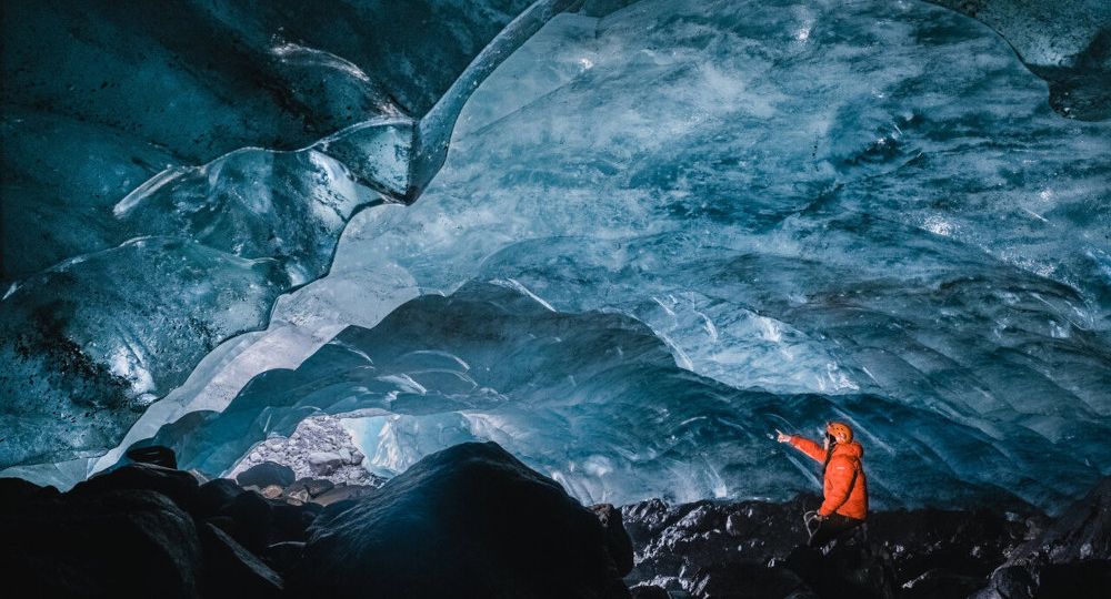 A person expering an ice cave from within and pointing to the cave opening.