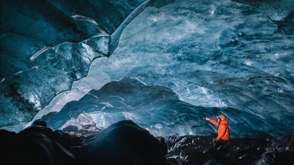 A person expering an ice cave from within and pointing to the cave opening.