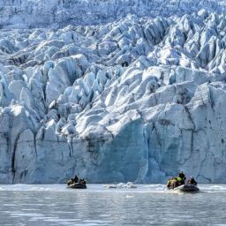 inflatable boats sailing on a glacial lagoon close up to the glacier wall.