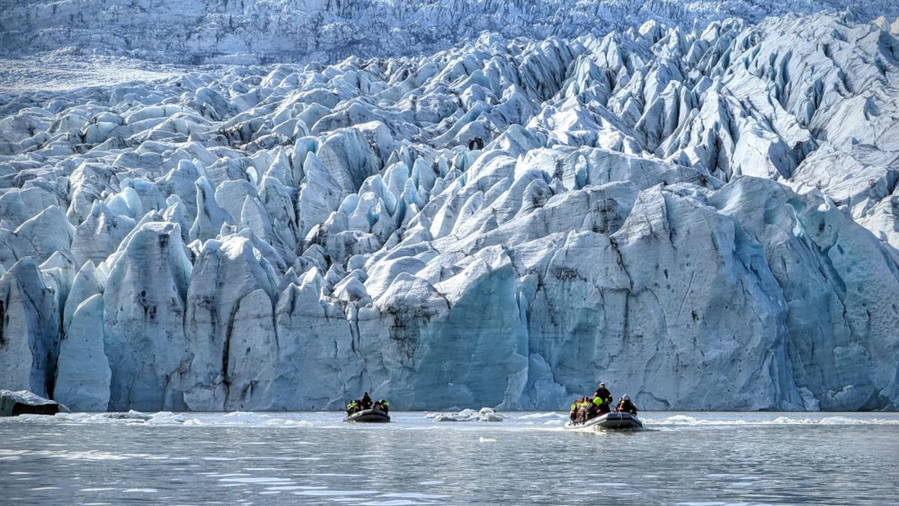 inflatable boats sailing on a glacial lagoon close up to the glacier wall.