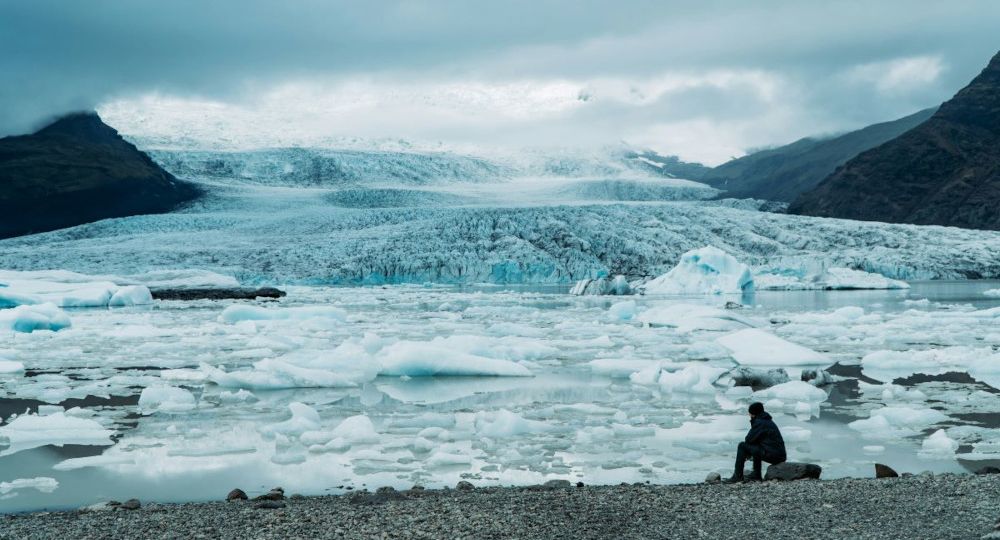 A person sits by the shore at Fjallsárlón glacial lagoon, with many icebergs floating around in the lagoon.