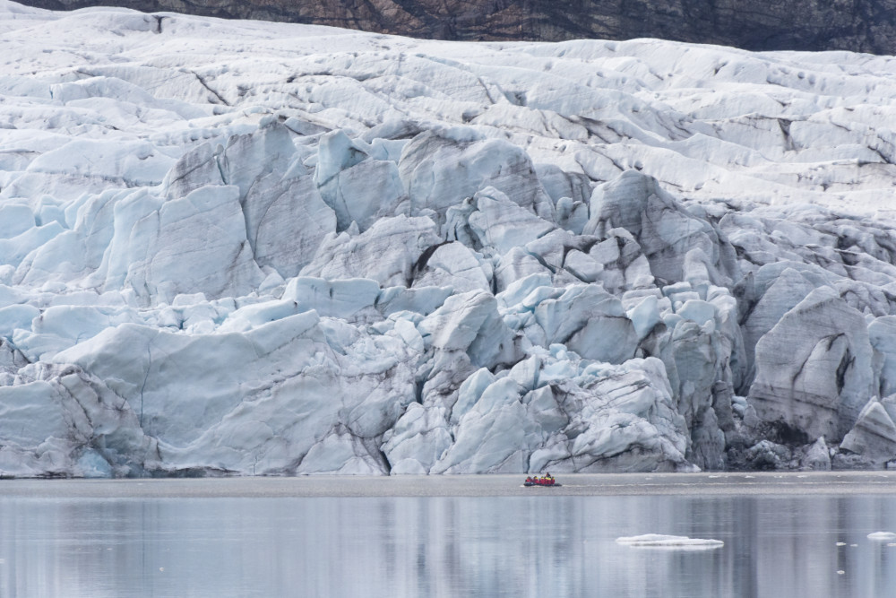 inflatable boat sailing on glacial lagoon, close up to the glacier wall and looking is looking small.