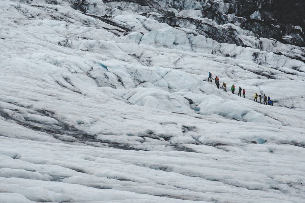 Group of people walking in a line, on a glacier.