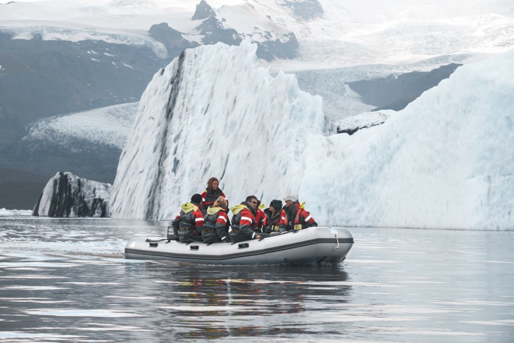 Inflatable boat on Fjallsarlón glacial lagoon with group of people, close by a big white iceberg.