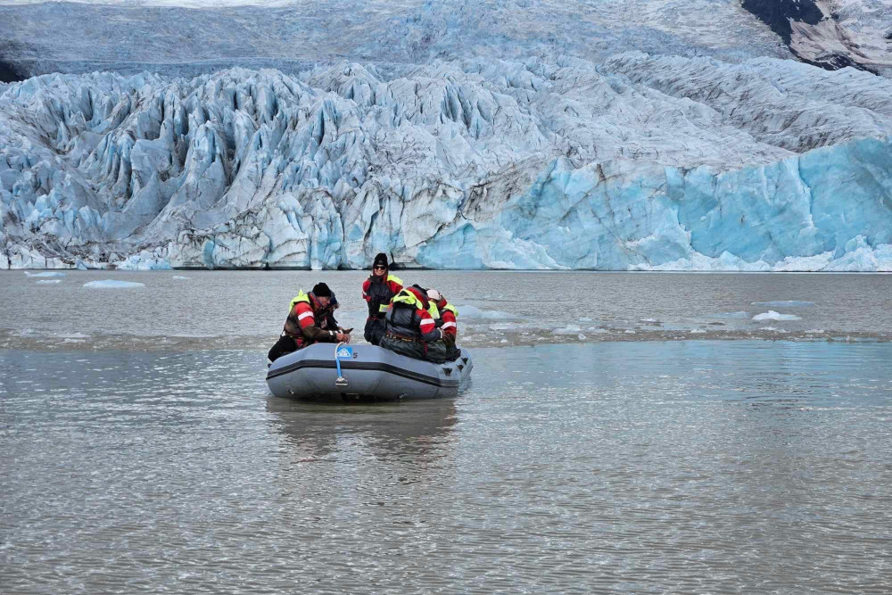 People in an inflatable boat at Fjallsárlón glacial lagoon, with Fjallsjökul glacier in the background.