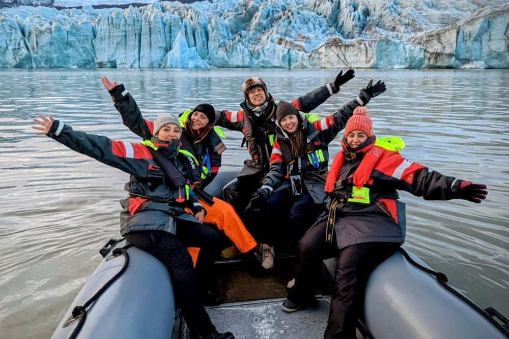 Small group of people waving and enjoying iceberg boat tour, in front of a glacier.