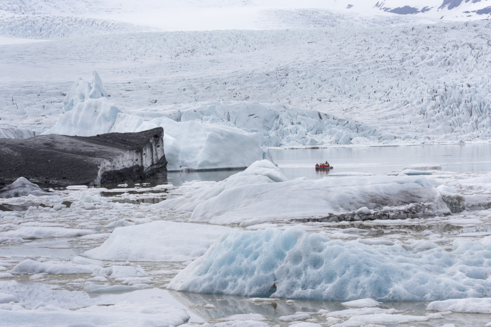 Inflatable boat on fjallsarlon glacial lagoon, in distance among floating icebergs.