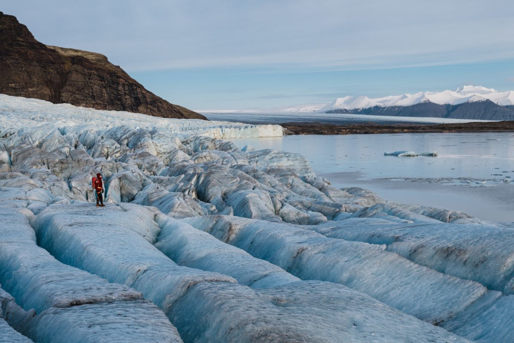 Person standing on Fjallsjokull with a view to Fjallsarlon and Breidarmerkurjokull glacier in far background.