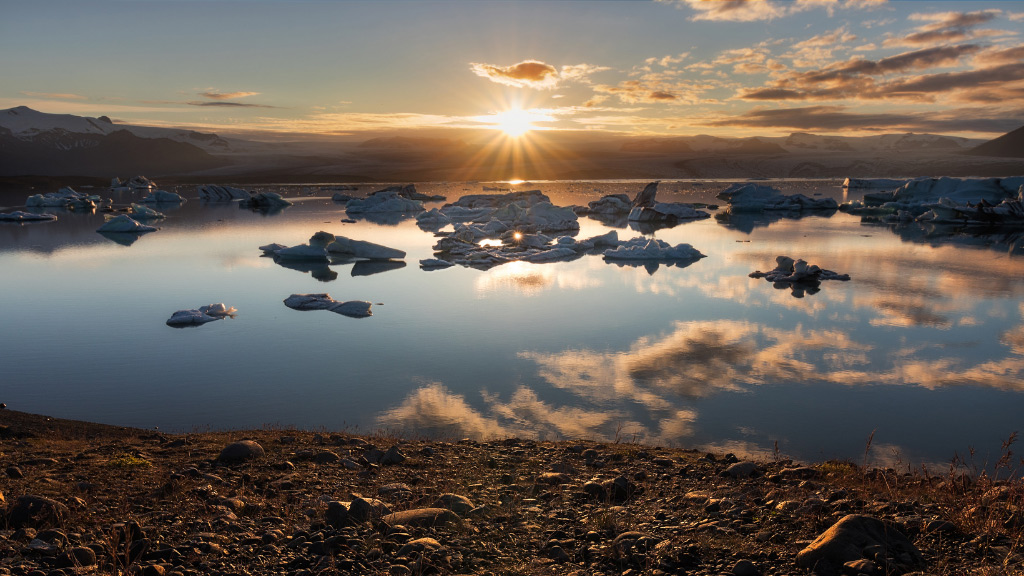 The midnight sun settling down over a glacier lagoon in Iceland.