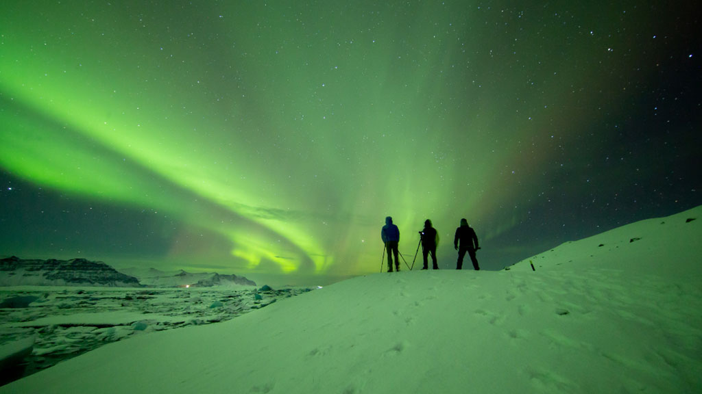 Three people taking pictures of the Northern lights in South Iceland with cameras on tripods.