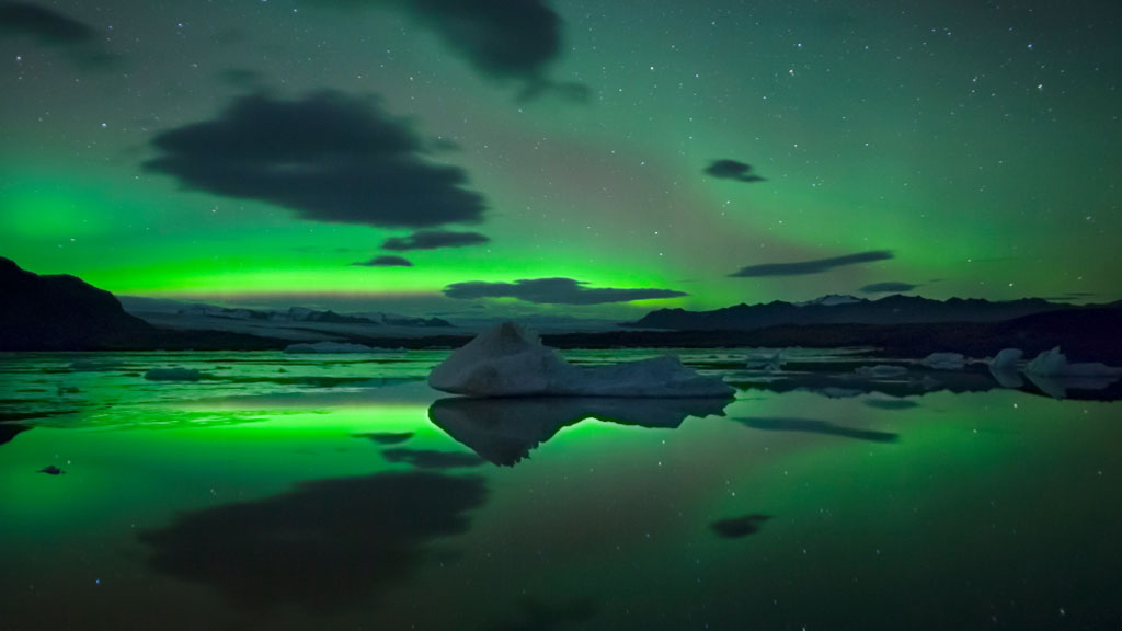 The Northern lights above Fjallsárlón glacier lagoon and a large floating iceberg.