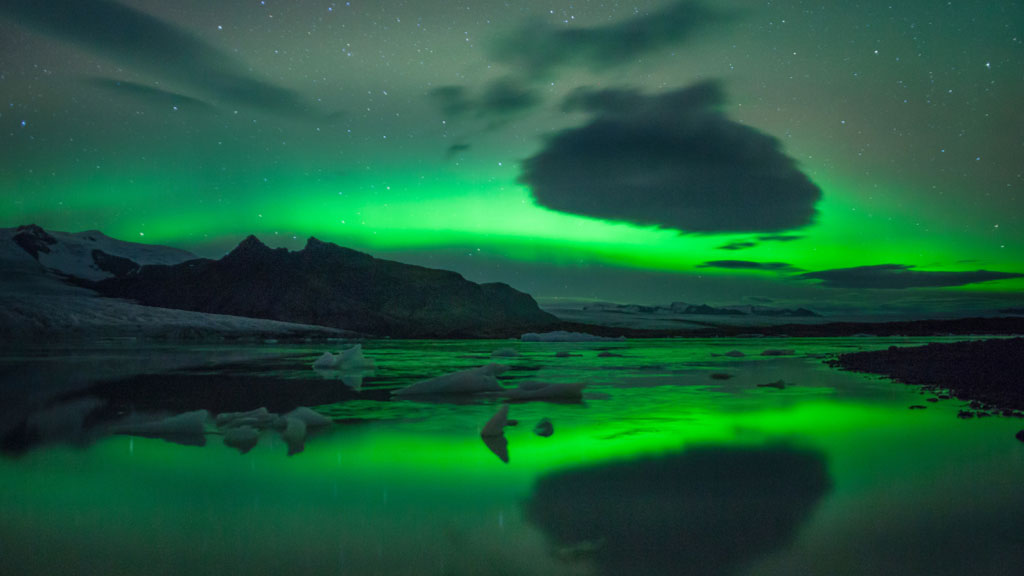 The Northern lights above Fjallsárlón glacier lagoon with a perfect reflection of the lights on the lagoon surface and floating ice bergs.