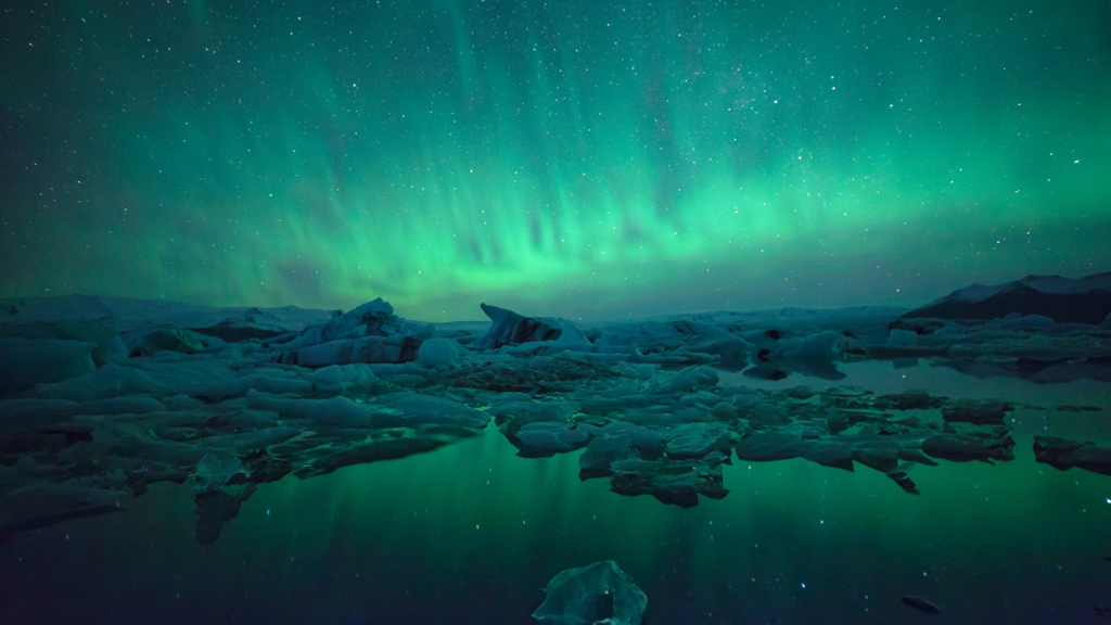 The Northern Lights hovering above Jökulsárlón glacier lagoon with floating ice bergs on the lagoon.