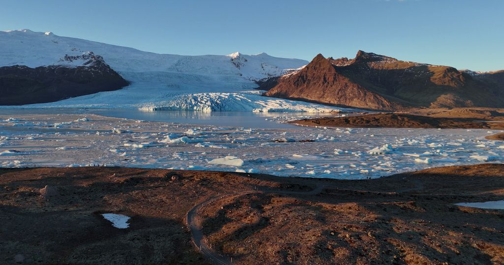 An overview picture of Fjallsárlón glacier lagoon, Fjallsjökull glacier, and towering mountains.