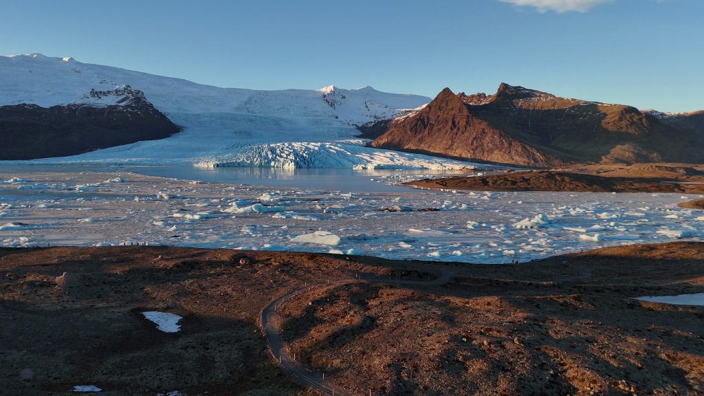 An overview picture of Fjallsárlón glacier lagoon, Fjallsjökull glacier, and towering mountains.