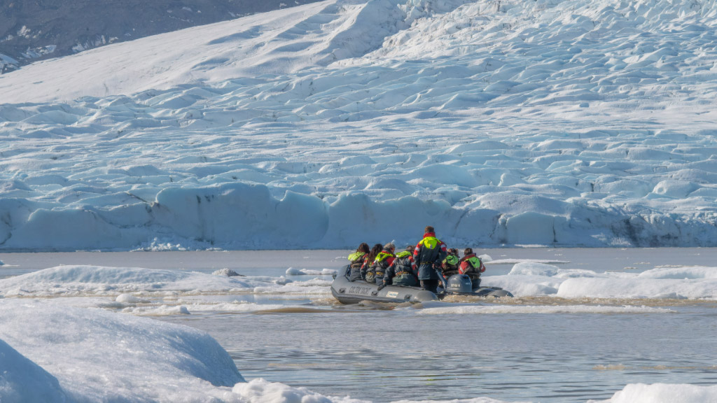 A group of people in an iceberg boat tour sailing past icebergs with the Fjalljökull glacier in the background.