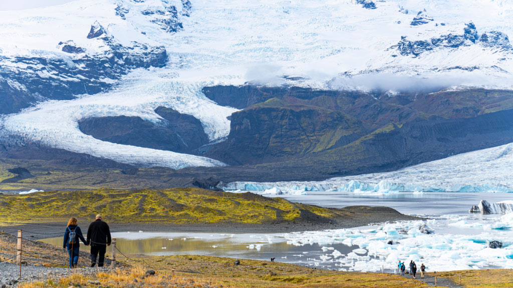 People walking on a walking path in front of Fjallsjökull glacier and Fjallsárlón glacier lagoon.
